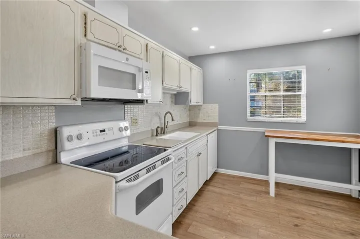 Kitchen with white appliances, backsplash, light countertops, light wood-type flooring, and recessed lighting