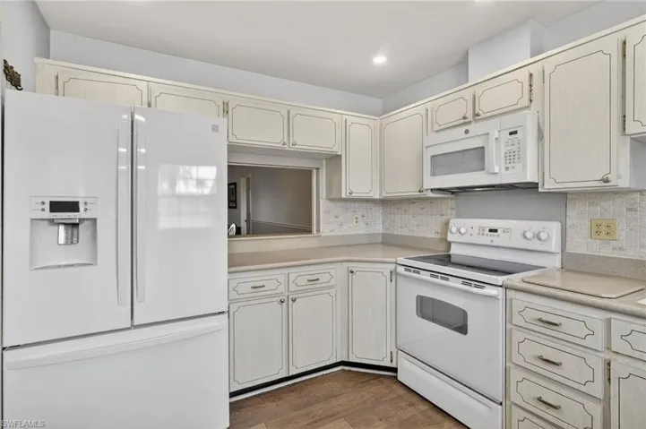 Kitchen with white appliances, light countertops, dark wood-style flooring, backsplash, and recessed lighting