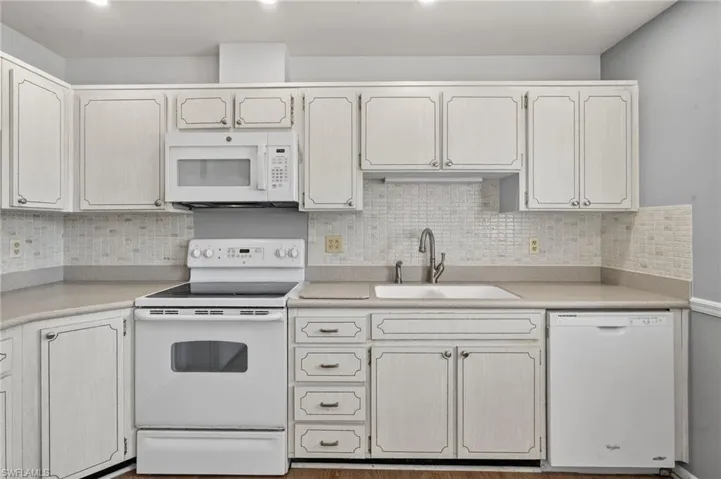 Kitchen with white appliances, backsplash, light countertops, and recessed lighting