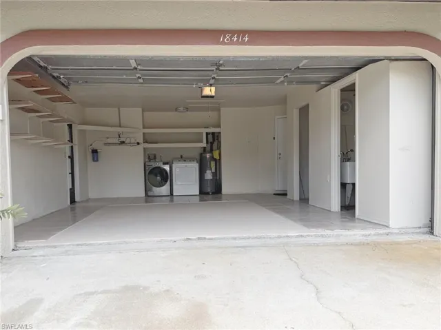 Spacious garage featuring a finished floor, built-in shelving, a dedicated laundry area with washer and dryer hookups, and a water heater