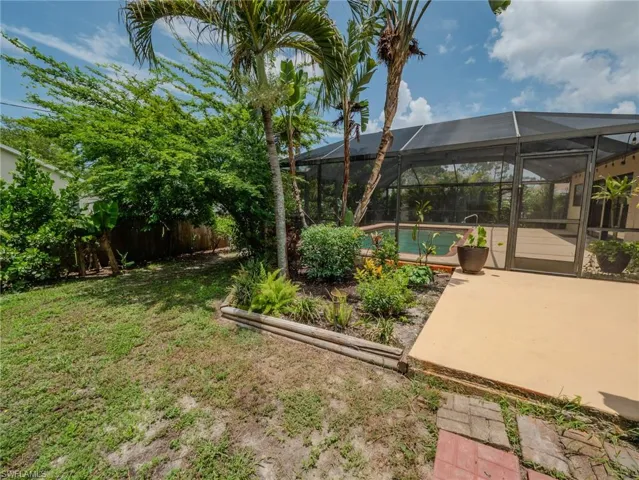 Screened outdoor swimming pool enclosure with a surrounding deck, complemented by a landscaped garden bed featuring palm trees and diverse plantings