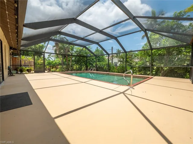 Screened pool enclosure featuring a rectangular swimming pool with brick coping, a large concrete deck, and perimeter landscaping