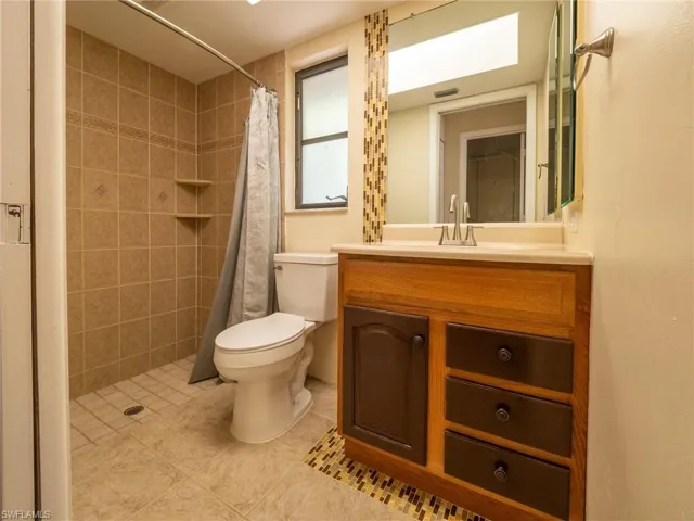 Bathroom featuring a walk-in shower with tile surround, a single vanity with a light wood-tone cabinet and contrasting drawer fronts, a solid surface countertop, and a built-in window