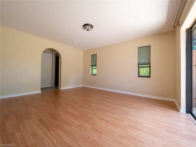 Spacious room featuring wood-finish flooring, an arched doorway, and multiple windows with roller shades