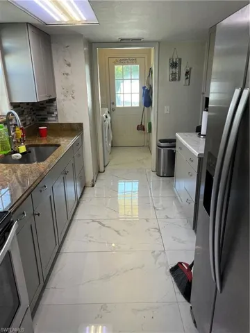 Kitchen with backsplash, gray cabinets, fridge, sink, and independent washer and dryer