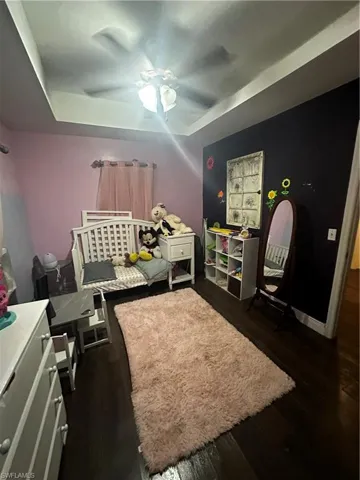 Bedroom featuring dark wood-type flooring, ceiling fan, and a raised ceiling