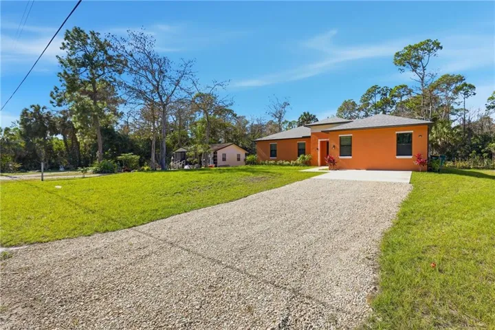 Ranch-style home featuring gravel driveway, a front lawn, and stucco siding