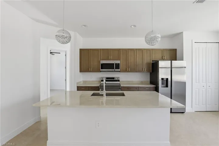 Kitchen with appliances with stainless steel finishes, light stone counters, a kitchen island with sink, pendant lighting, and recessed lighting