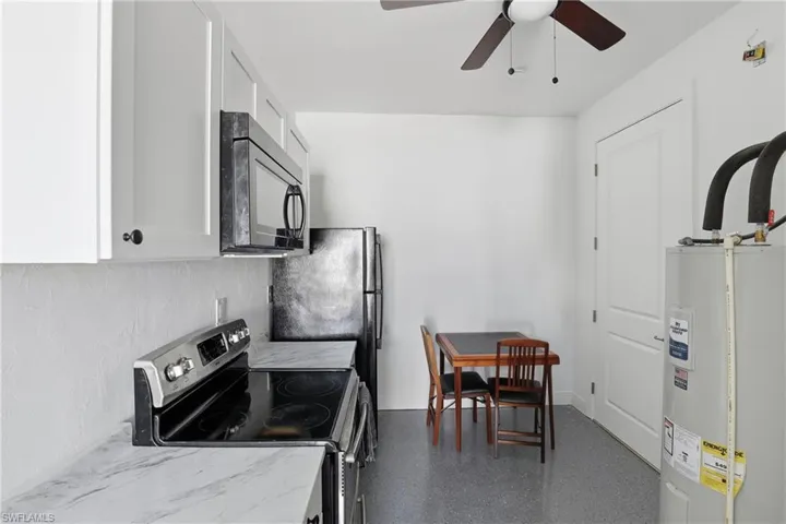 Kitchen with stainless steel range with electric cooktop, black microwave, water heater, white cabinets, and a ceiling fan