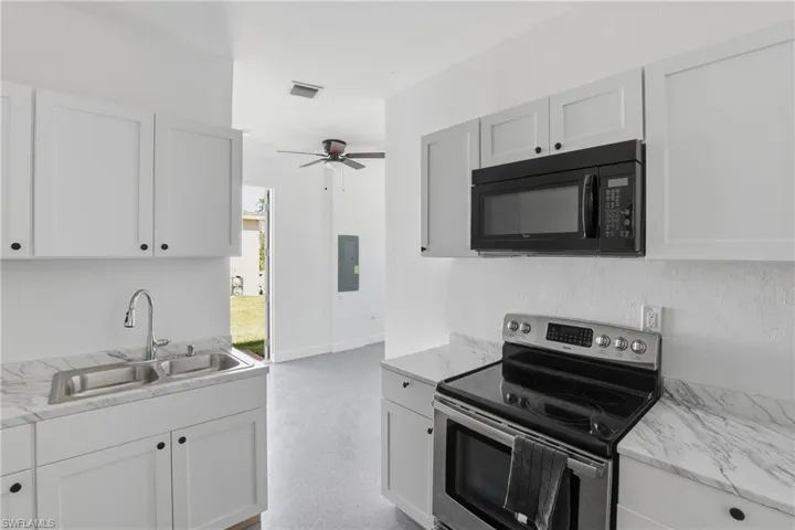 Kitchen with electric range, black microwave, and white cabinetry