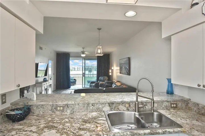 Kitchen with white cabinetry, open floor plan, a ceiling fan, and light stone counters
