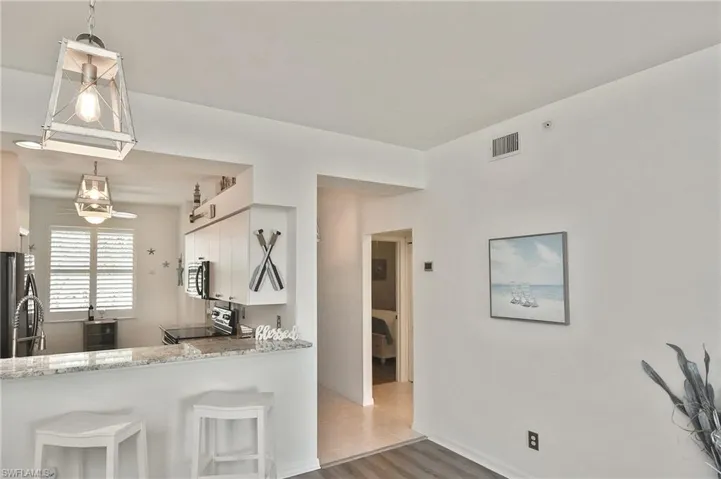 Kitchen featuring white cabinets, a kitchen bar, pendant lighting, light stone countertops, and stainless steel appliances