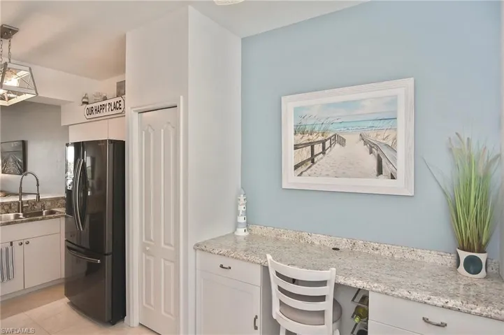 Kitchen featuring black refrigerator with ice dispenser, built in desk, light stone countertops, hanging light fixtures, and light tile patterned floors