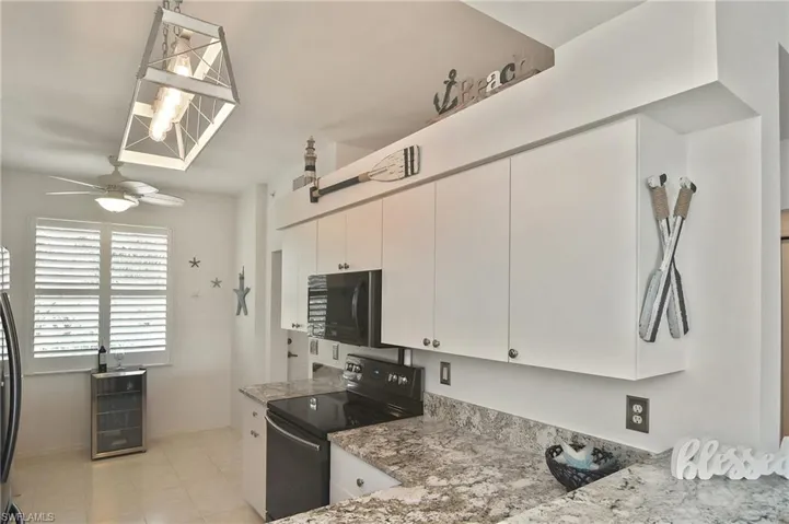 Kitchen with black electric range, light stone counters, ceiling fan, white cabinetry, and light tile patterned floors