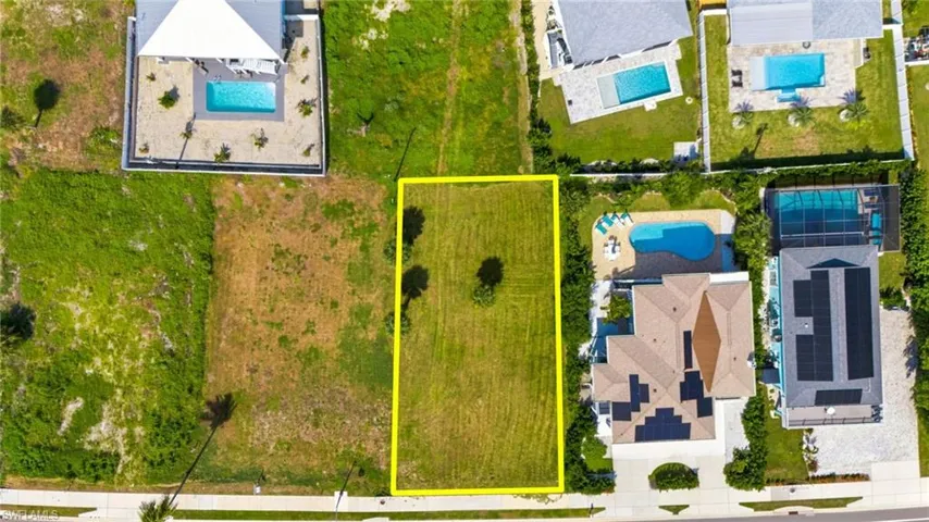 Vacant residential lot featuring an open grass lawn, established palm trees, and street-front access - Virtually Edited Image