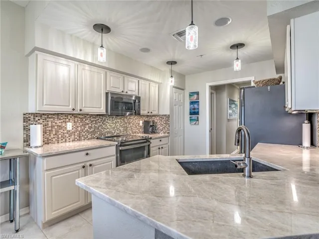 Kitchen featuring light stone countertops, stainless steel appliances, white cabinetry, pendant lighting, and tasteful backsplash