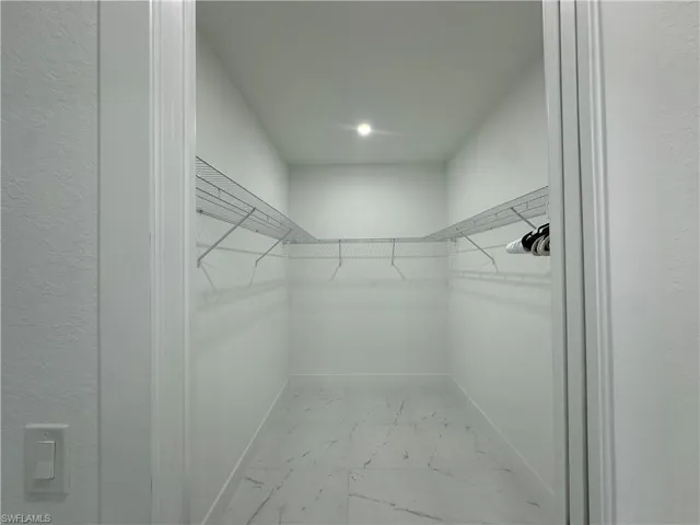 Spacious walk-in closet featuring white wire shelving, a recessed ceiling light, and marble-look floor tiling