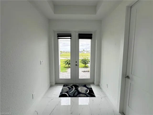 Entryway featuring double French doors, large format tile flooring, a tray ceiling, and white panel doors