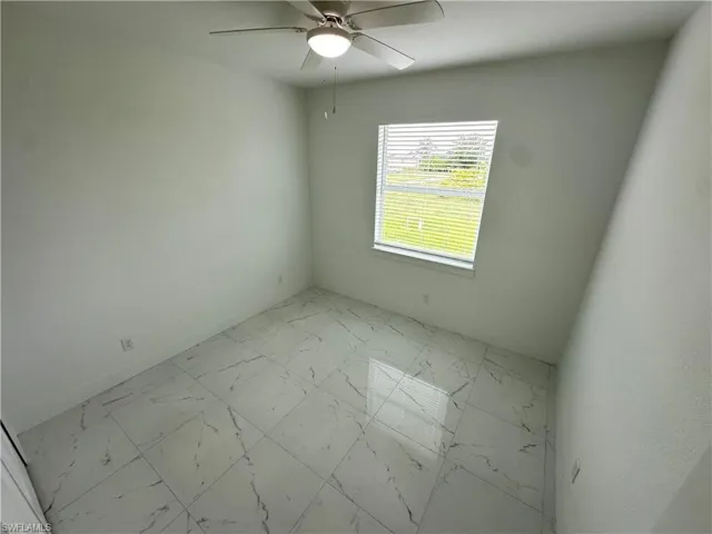 Room featuring a ceiling fan with integrated lighting, large window with blinds, and white square floor tiles with grey veining
