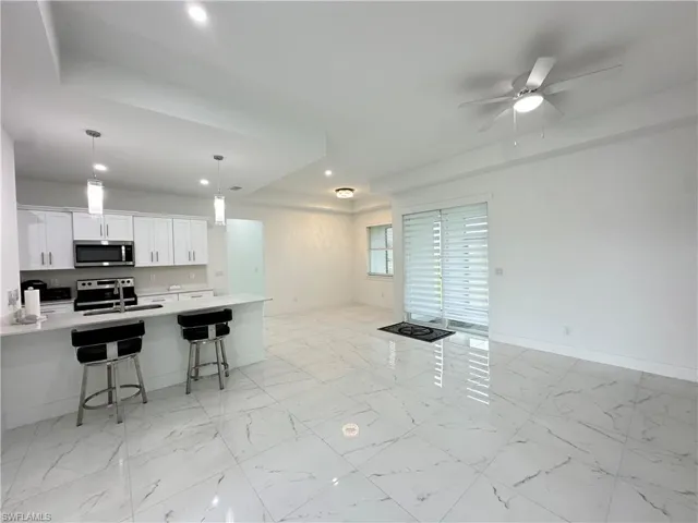 Open-concept living space featuring high ceilings, large format tile flooring, a contemporary kitchen with white cabinetry and stainless steel appliances, a kitchen island with pendant lighting, and sliding glass doors