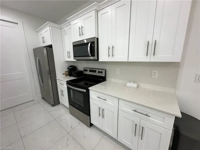 White shaker-style cabinetry with crown molding, stainless steel appliances, speckled solid surface countertops, and a coordinating backsplash