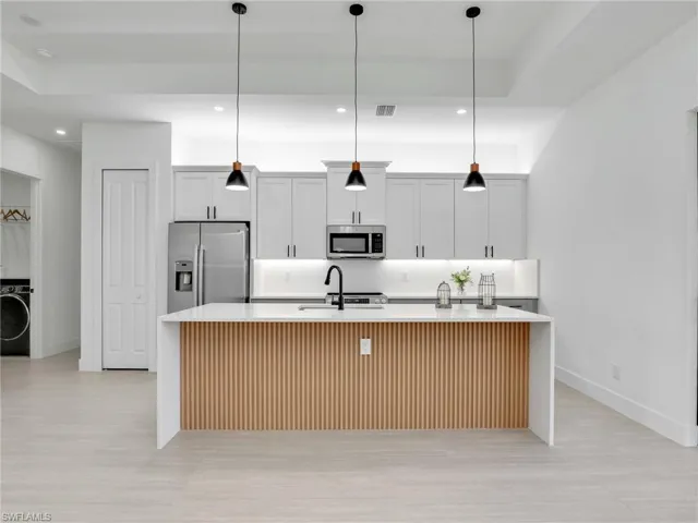 Kitchen with a large island with sink, appliances with stainless steel finishes, recessed lighting, light stone counters, and white cabinets