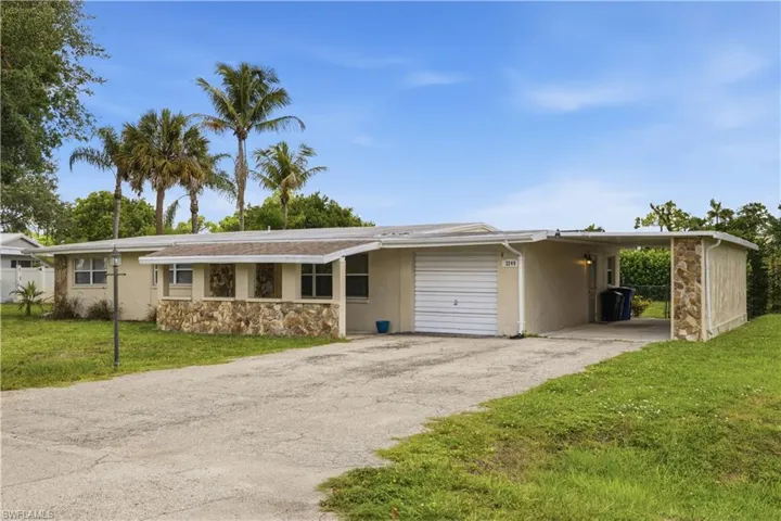 Single-story residence featuring a concrete driveway, an attached garage, a covered carport, and decorative stone accents on the facade