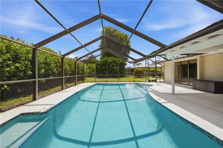 Screened outdoor pool area featuring a blue-tiled swimming pool with integrated steps, a surrounding concrete deck, and a covered patio area with sliding glass doors leading indoors