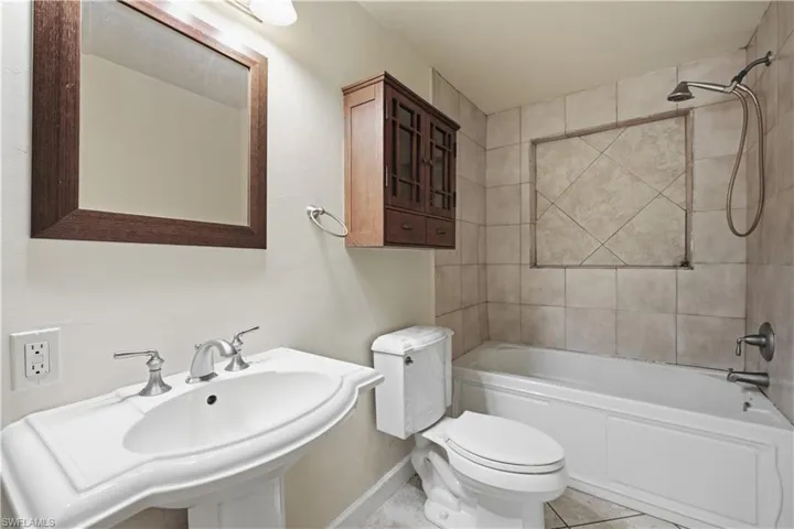 Pedestal sink with brushed nickel faucet, framed mirror, and warm-toned wall cabinetry