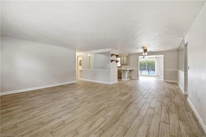 Spacious interior featuring wood-finish tile flooring, neutral wall tones, a ceiling fan, and a pass-through kitchen opening to a window overlooking a swimming pool
