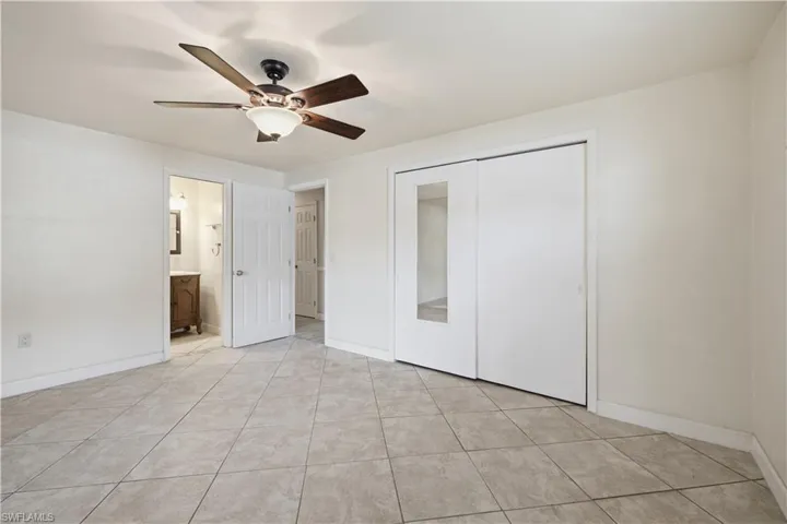 Spacious room featuring neutral painted walls, ceramic tile flooring, a ceiling fan with light fixture, and a white sliding closet door with a full-length mirror panel
