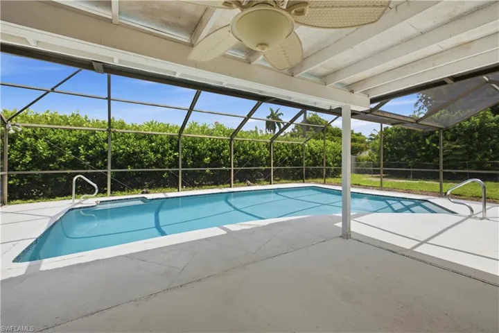 Screened patio featuring a swimming pool with integrated steps, a ceiling fan, and a privacy hedge