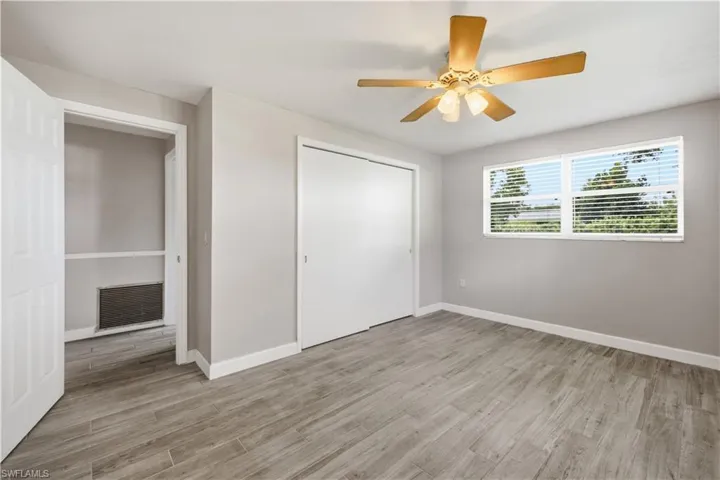 Spacious room featuring wood-finish flooring, light gray walls, a ceiling fan with light fixture, and a window with horizontal blinds