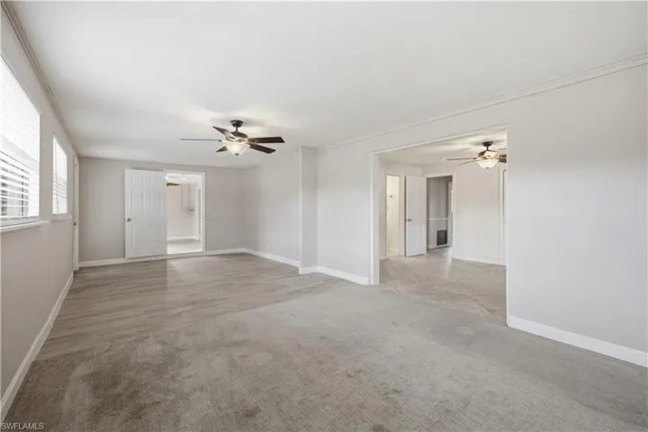 Spacious room featuring light gray carpeting, wood-finish flooring, two windows with blinds, two ceiling fans, and a sliding double door