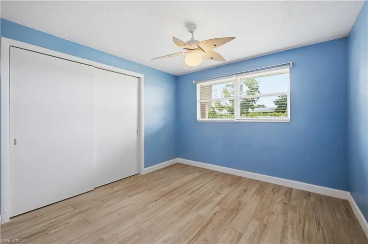 Room featuring wood-finish flooring, a ceiling fan with integrated lighting, a window with blinds, and white sliding closet doors