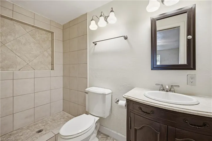 Bathroom featuring a tiled shower with a recessed shelf, a traditional dark wood vanity with a white countertop, an oval undermount sink, and a framed mirror