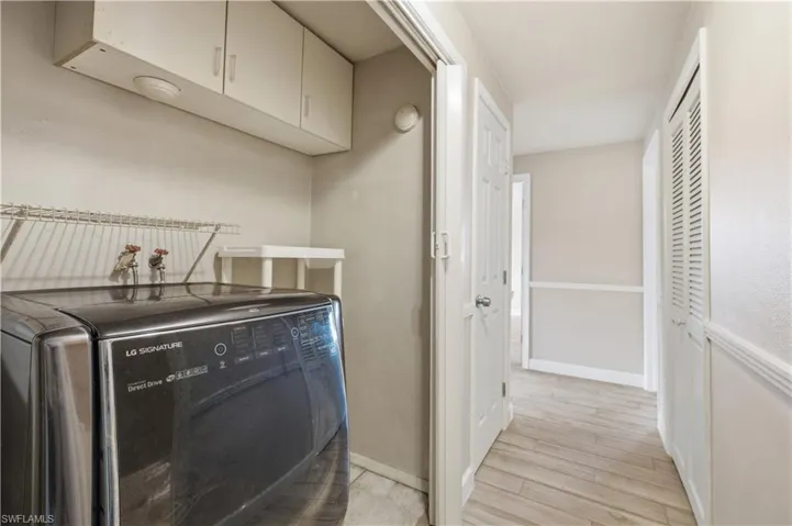 Dedicated laundry area featuring overhead cabinetry, wall-mounted shelving, and wood-look flooring extending into the hallway