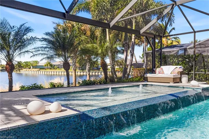 View of pool with pool water feature, glass enclosure, a water view, and a jacuzzi