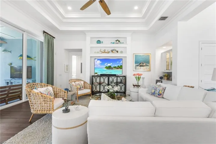 Living room with built in shelves, dark hardwood / wood-style flooring, ceiling fan, and ornamental molding