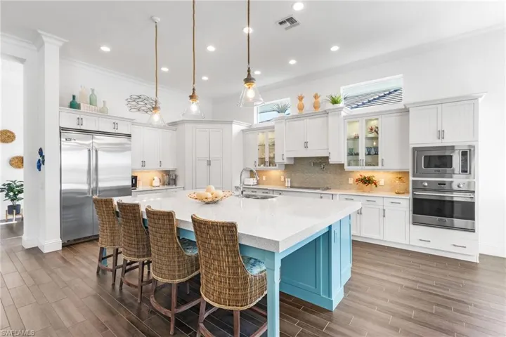 Kitchen with a large island, sink, built in appliances, decorative light fixtures, and a kitchen bar