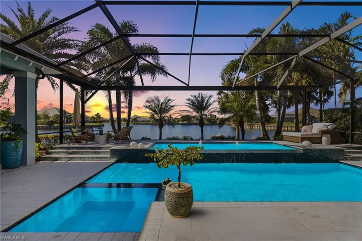 Pool at dusk with glass enclosure, a patio area, and a water view