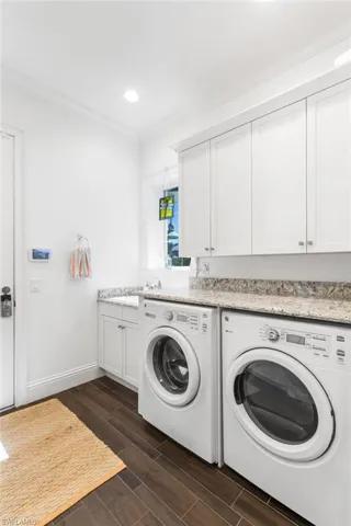 Clothes washing area featuring sink, cabinets, dark hardwood / wood-style floors, crown molding, and washer and clothes dryer