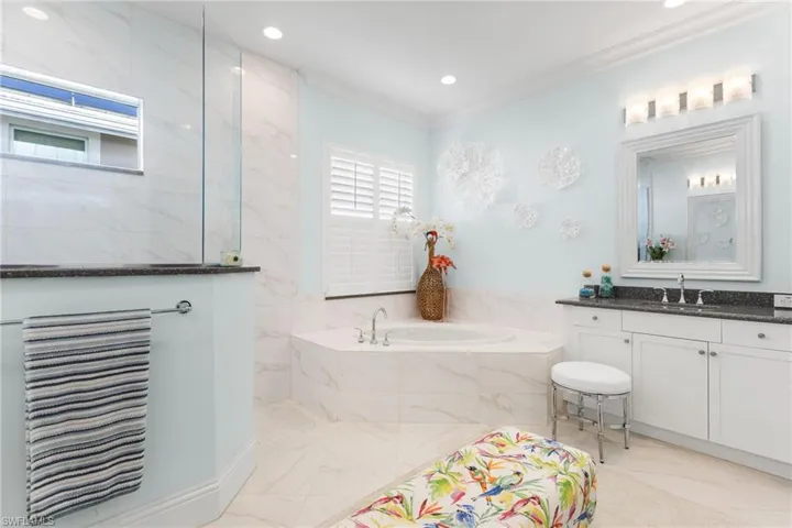 Bathroom with tiled bath, a wealth of natural light, crown molding, and vanity