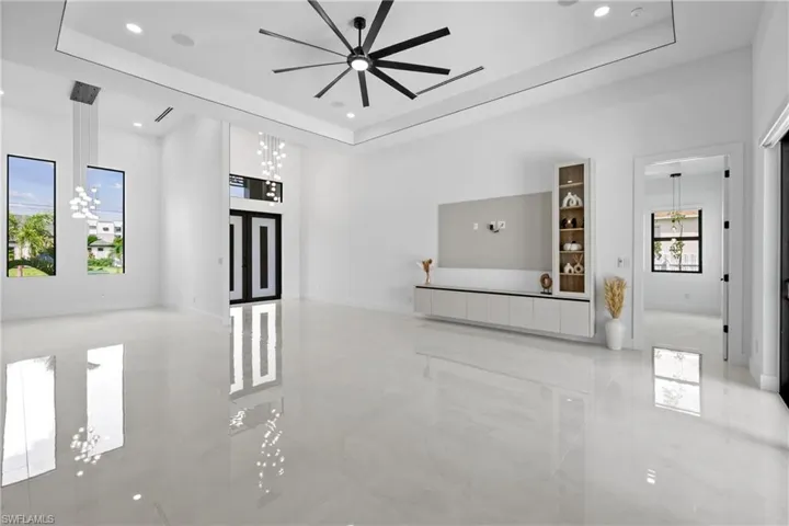 Unfurnished living room with a raised ceiling, ceiling fan, recessed lighting, and a chandelier
