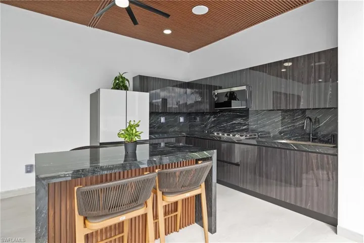 Kitchen with modern cabinets, tasteful backsplash, dark stone countertops, and a kitchen bar