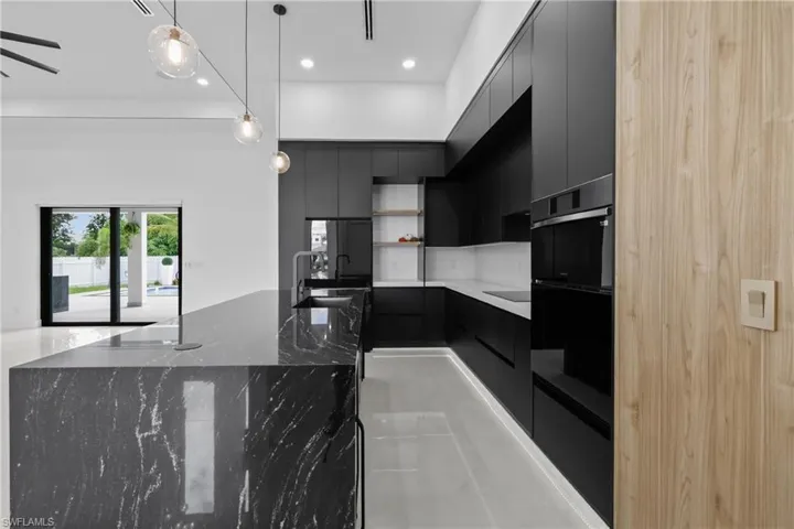 Kitchen featuring modern cabinets, dark cabinets, black appliances, hanging light fixtures, and recessed lighting