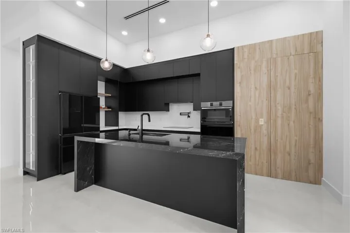 Kitchen with modern cabinets, dark cabinets, dark stone counters, a center island with sink, and pendant lighting