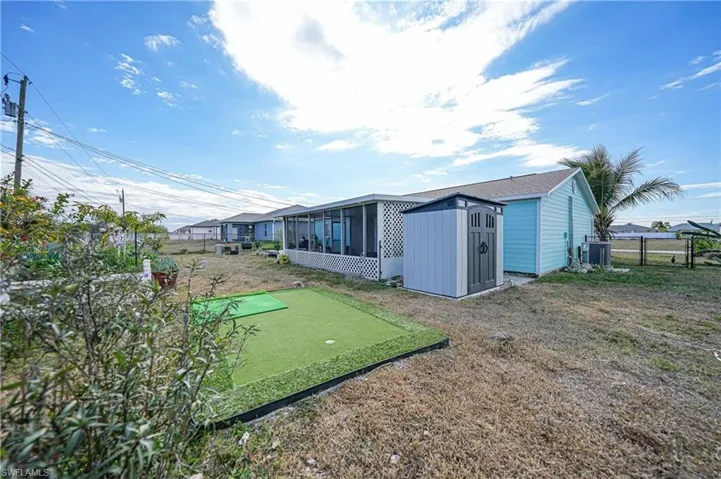 Fenced backyard featuring an area to practice putting, a sunroom, and a storage shed