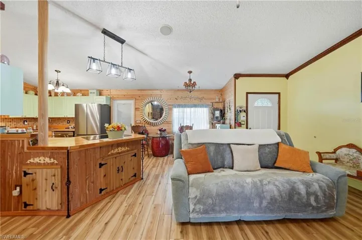 Living area with a chandelier, crown molding, a textured ceiling, light wood-type flooring, and wood walls