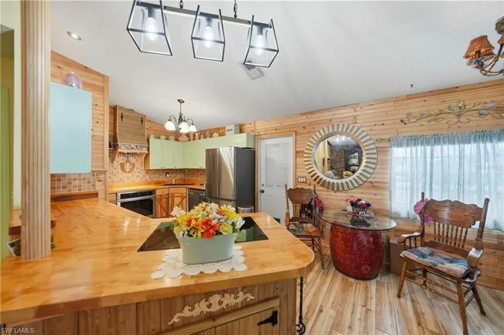 Kitchen with a peninsula, hanging light fixtures, vaulted ceiling, light wood finished floors, and stainless steel appliances